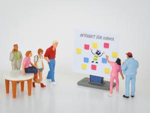 Seitenstarke Fortbildungen zum Thema Kinderwebseiten Miniatur-Menschen stehen vor einem Pinboard einer Schulung