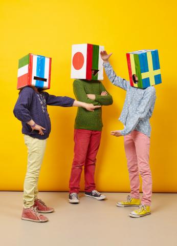 Drei Kinder haben angemalte Kartons mit Flaggen verschiedener Länder auf dem Kopf