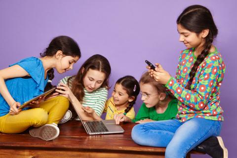 Fünf Mädchen schauen auf ein Smartphone, ein Tablet und ein Laptop