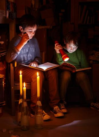 Zwei Kinder lesen mit Taschenlampen und Kerzenlicht im Dunkeln Bücher