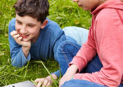 Müssen wir uns hier anmelden? Ein Junge und ein Mädchen sitzen im Gras an einem Laptop