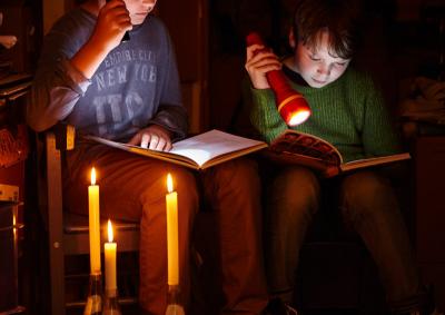 Zwei Kinder lesen mit Taschenlampen und Kerzenlicht im Dunkeln Bücher